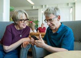 A man and a woman sitting next to each and looking at a mobile phone the man is holding