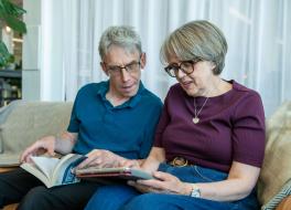 A man and a woman sitting next to each and looking at a tablet the woman is holding