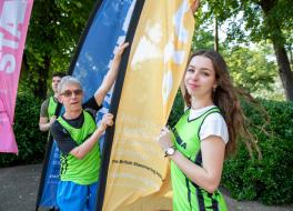 A man and a woman in running vests holding a flag and looking at the camera