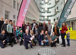 A group of people, some standing and some kneeling, all looking at the camera, some holding a flag
