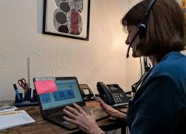 A woman sitting in front of a laptop computer and wearing a headset
