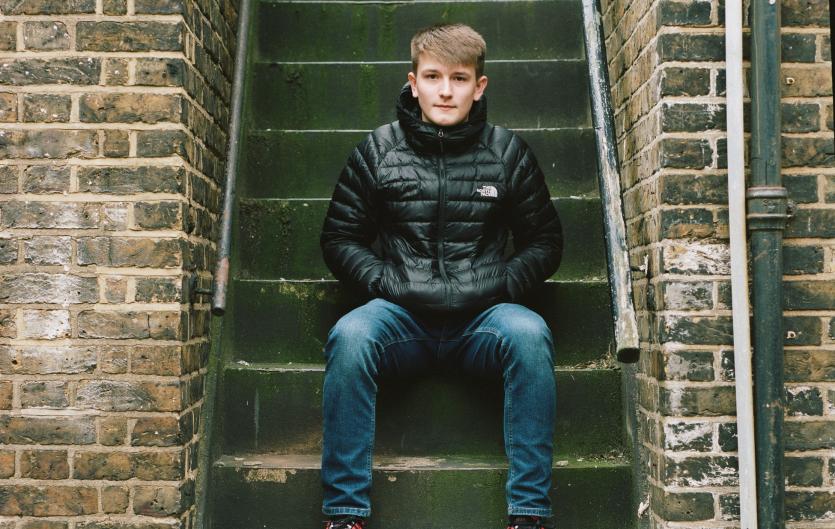 In education Teenage boy sitting on steps, looking intently at camera, hands in pockets