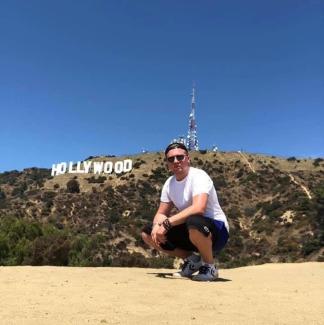 A man squatting with the Hollywood sign in the background