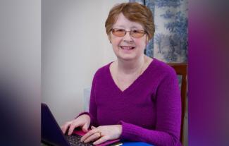 A woman typing on a laptop and smiling for the camera