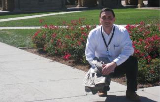 A man wearing a lanyard, kneeling in front of a flower bed