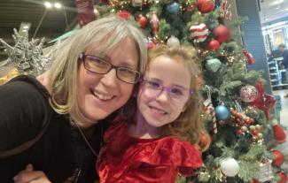 A woman and her young daughter looking at the camera and smiling, with a Christmas tree in the background.