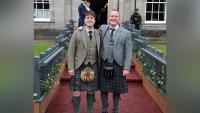 Two men in kilts standing together, looking at the camera and smiling