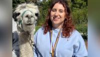 A young woman smiling and standing next to a llama