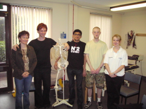Five people standing in a line and smiling for the camera, one of them resting his arm on a skeleton